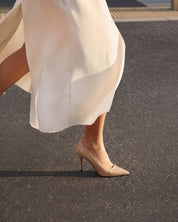 Beige high heeled shoes worn with a flowing white dress on a dark surface.