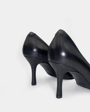 A pair of black leather high-heeled pumps shown from a rear three-quarter angle on a light gray studio background.