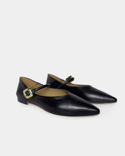 A pair of black leather pointed-toe Mary Jane flats with gold-tone buckle straps, displayed on a light gray background.