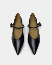 A pair of black leather pointed-toe Mary Jane pumps with gold-tone buckle straps, shown from a top-down view on a light gray background.