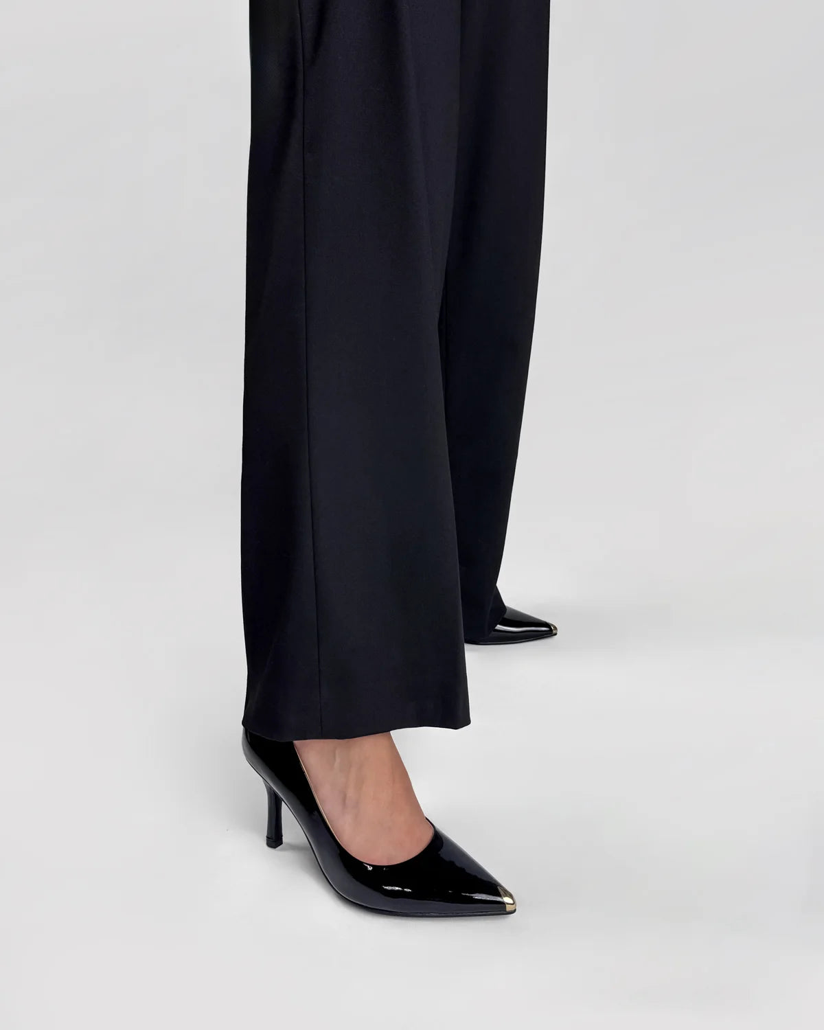 Black high-heeled shoes worn with black pants on a light gray background