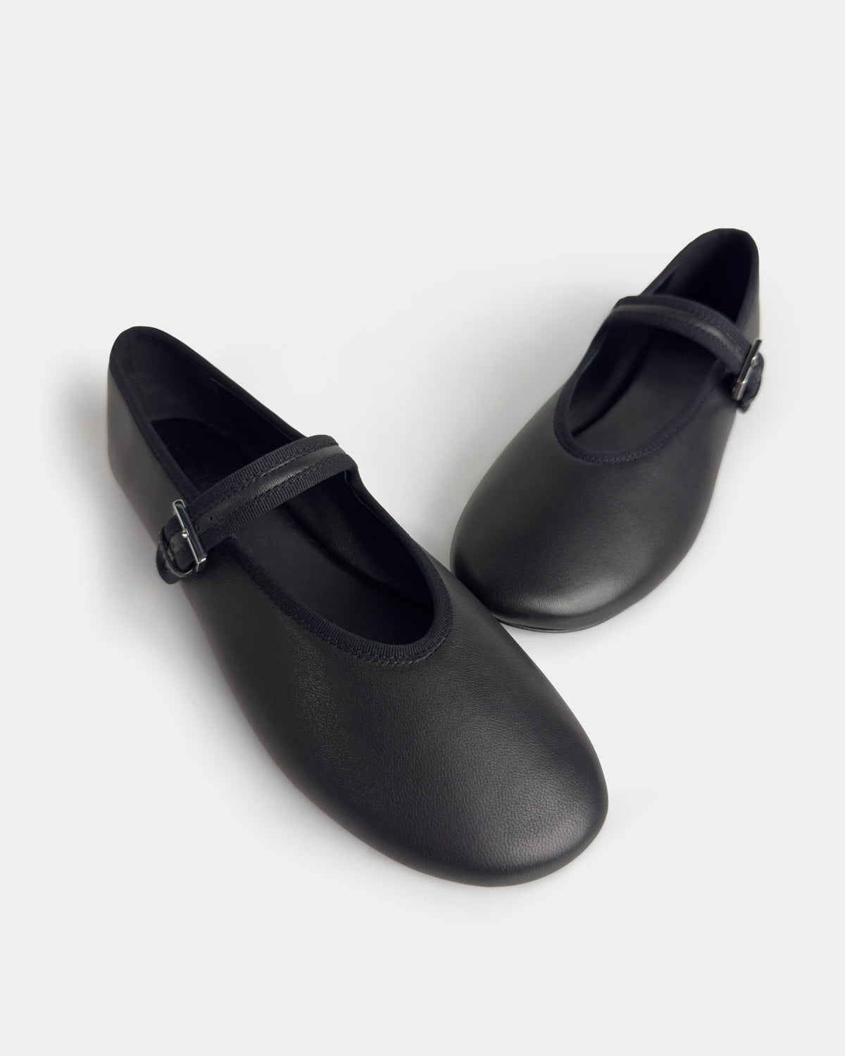 side view of a pair of black leather Mary Jane ballet flats with single strap and small buckle on the light grey background