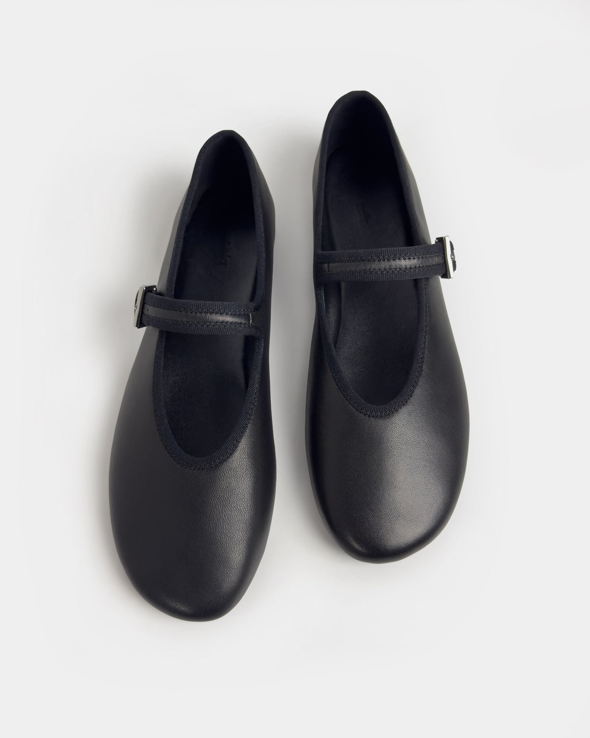 A pair of black leather ballet flats with a single strap and a small silver buckle, shown from a top-down view on a light gray background.
