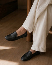 a person sitting somewhere comfortably in white pants and black sofe loafers