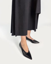Person wearing black pointed-toe kitten heels and a long black coat on a white background