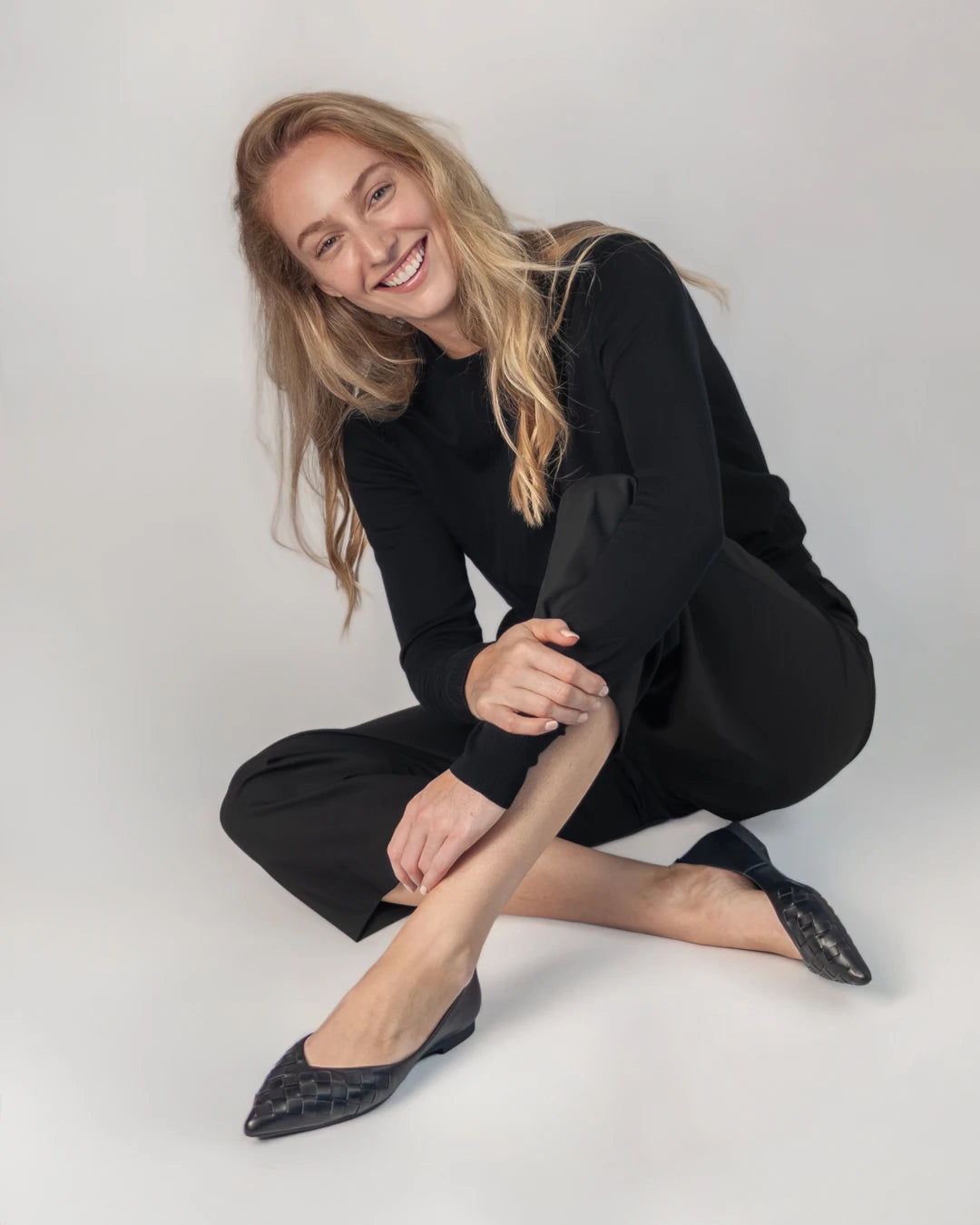 A woman wearing a black long-sleeve top and black pointed flats with a subtle dark pattern.