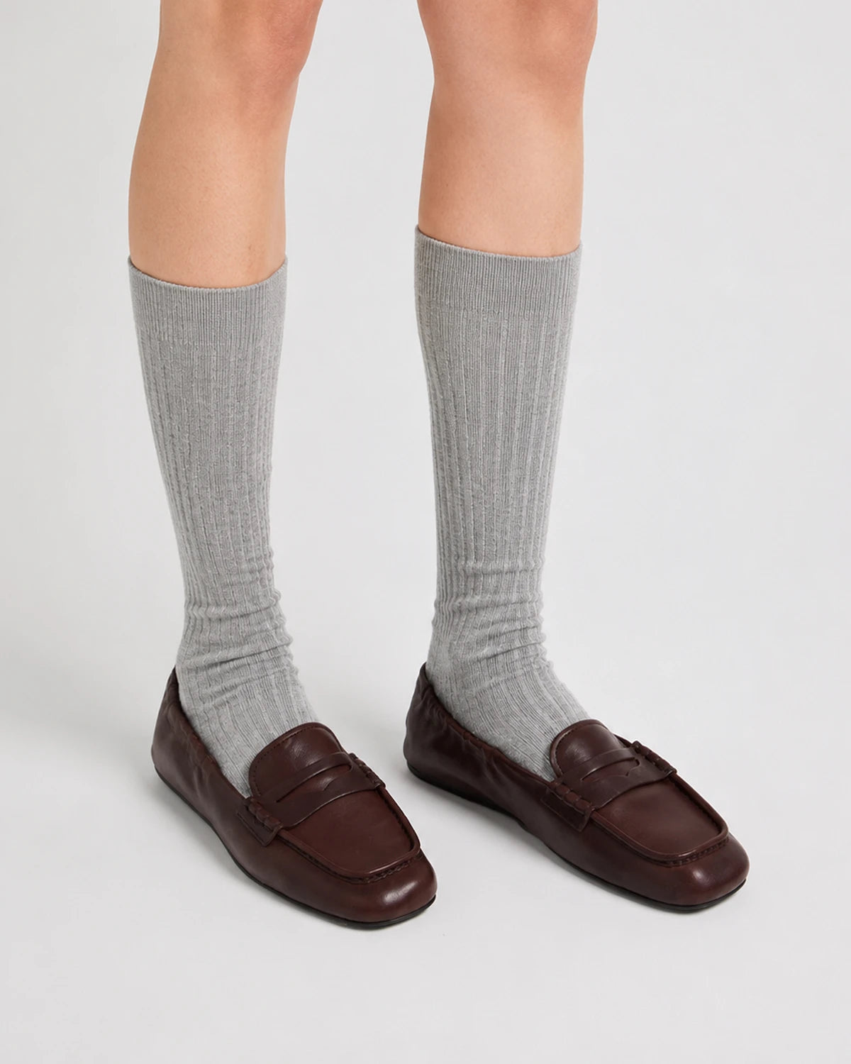 Person wearing gray knee-high socks and brown loafers on a light gray background