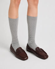 Person wearing gray knee-high socks and brown loafers on a light gray background