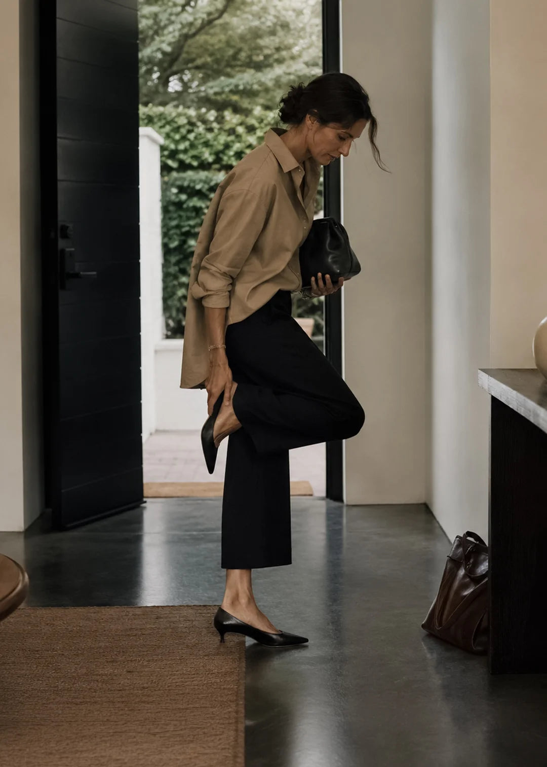 Woman in a beige shirt and black pants standing in a modern interior setting.