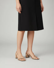 Woman wearing a black skirt and beige strappy sandals on a plain background