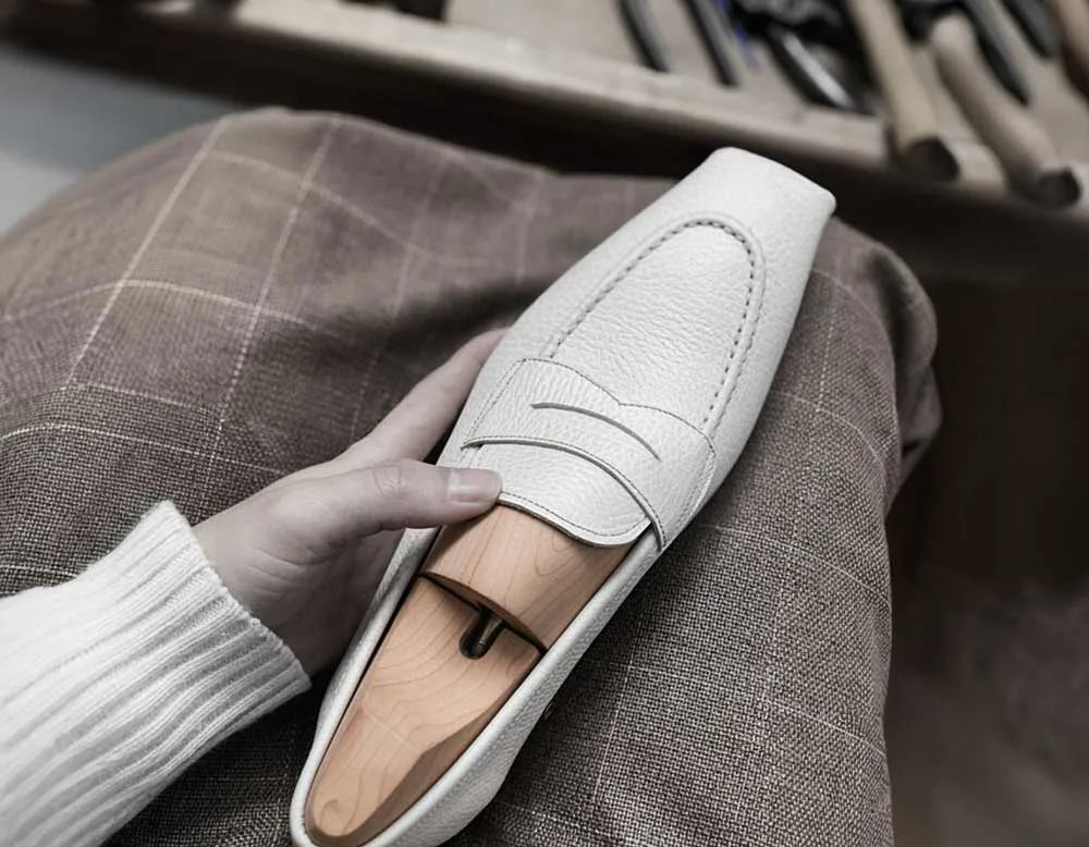 White loafer shoe held by a hand with a shoe making background