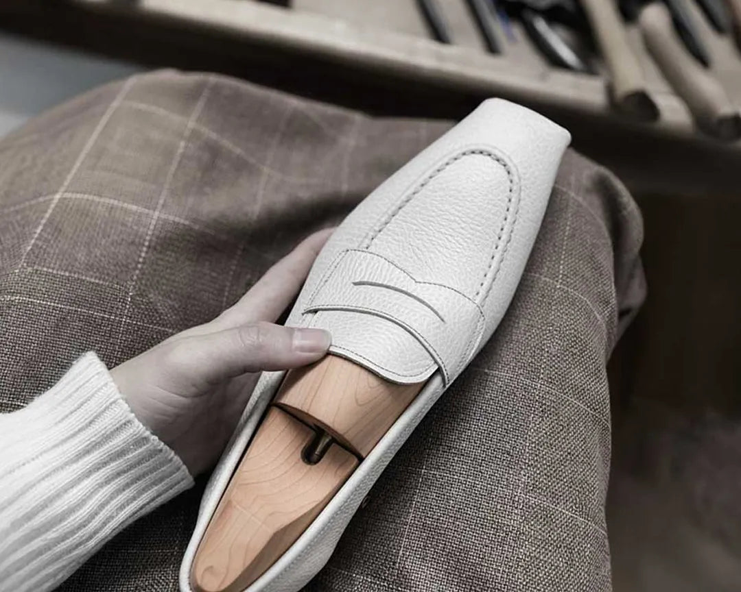White loafer shoe held by a hand with a shoe making background