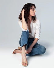 Woman wearing beige sandals with block heels and straps crafted with patent nude shade leather. 