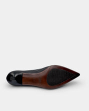 The outsole view of a pointed-toe shoe, showing a brown leather midsole with a black textured non-slip section and a glossy black toe cap, set against a light gray background.
