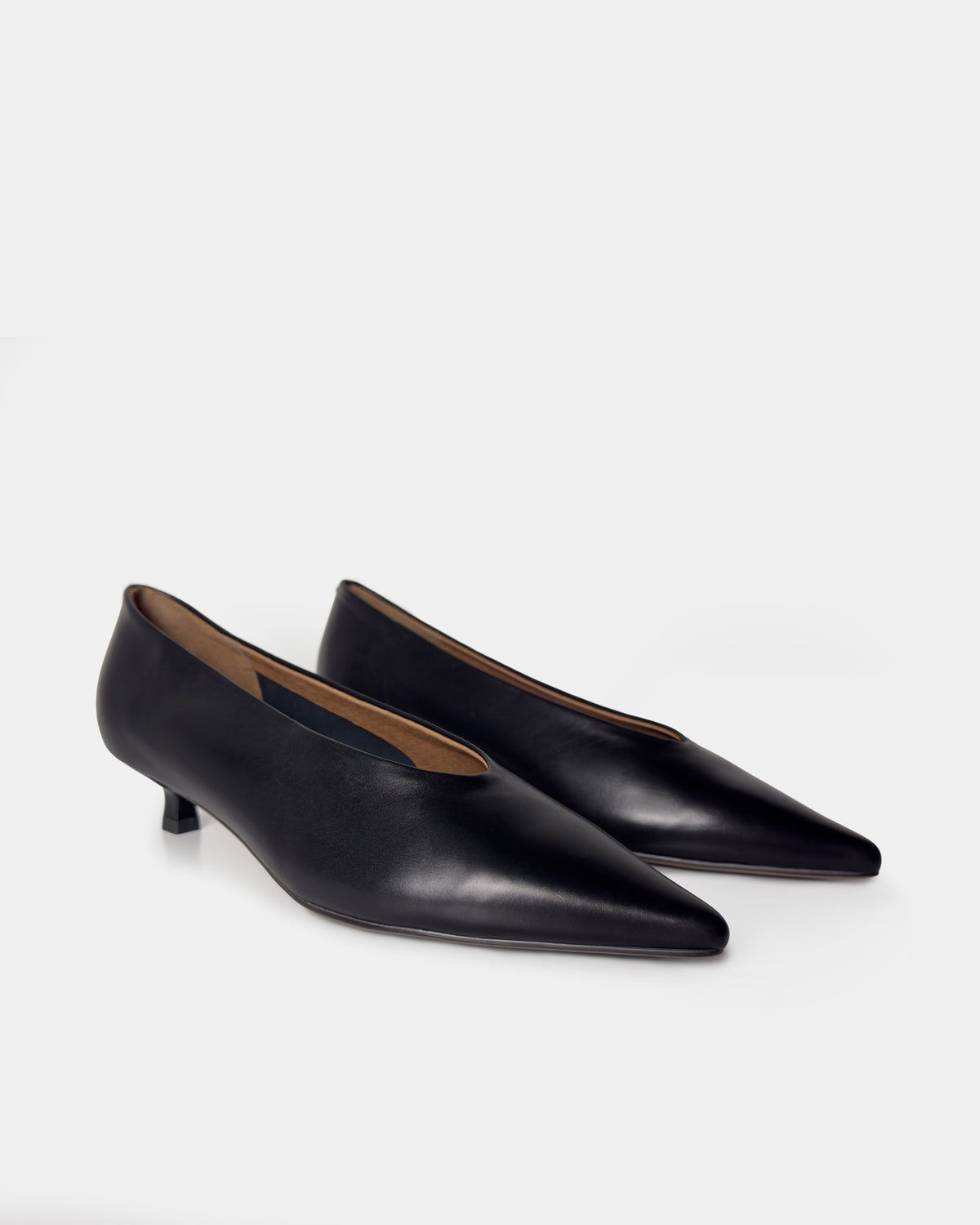A pair of black leather pointed-toe kitten heels on a light gray studio background.