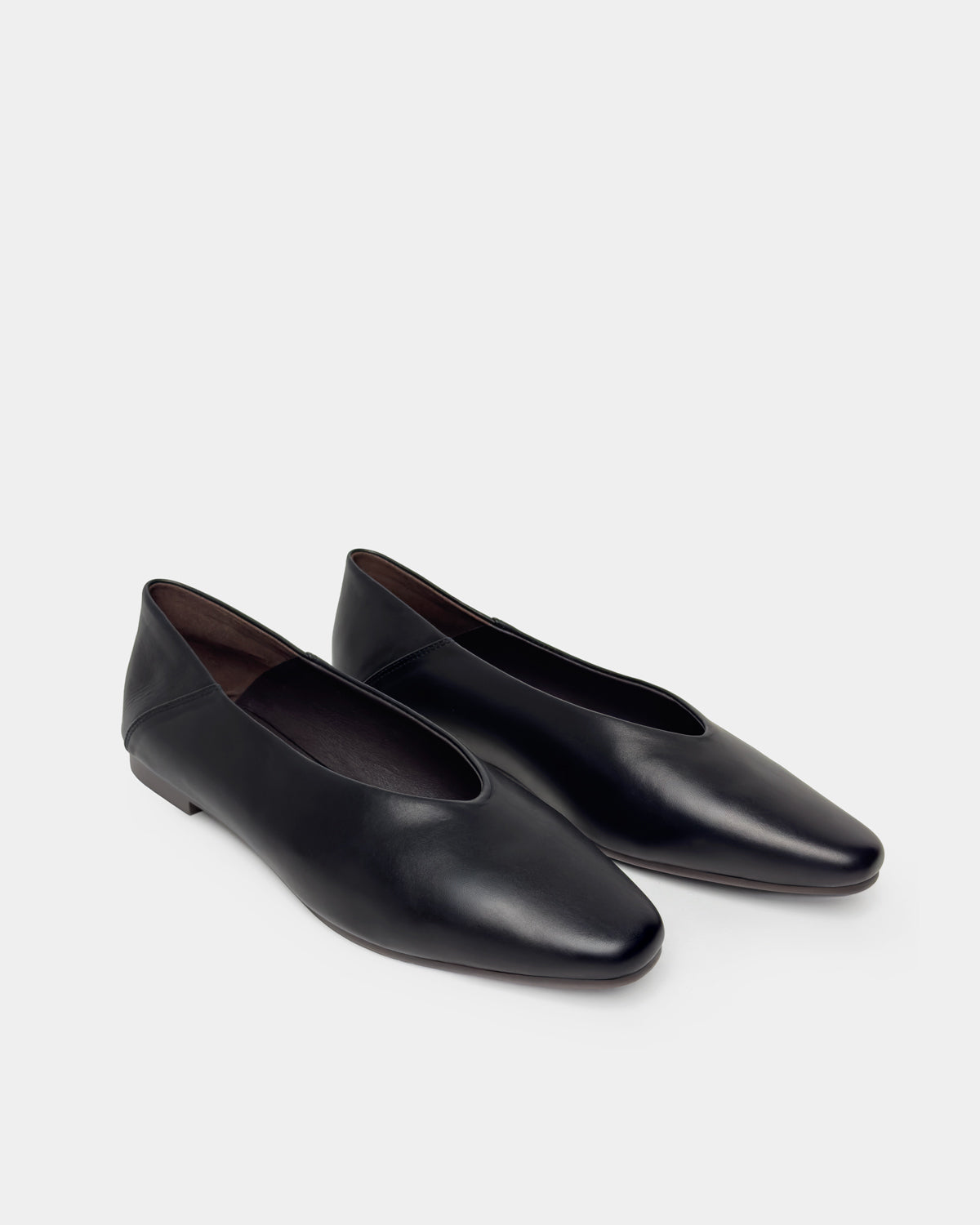 A pair of black leather slip-on flat shoes with round toes, shown from the front on a light gray background.