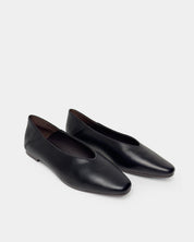 A pair of black leather slip-on flat shoes with round toes, shown from the front on a light gray background.