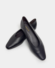 A pair of black leather round toe flats with a low block heel, displayed on a clean light gray background. The brand name 'ellementa' is printed in gold on the inner sole of the front shoe.
