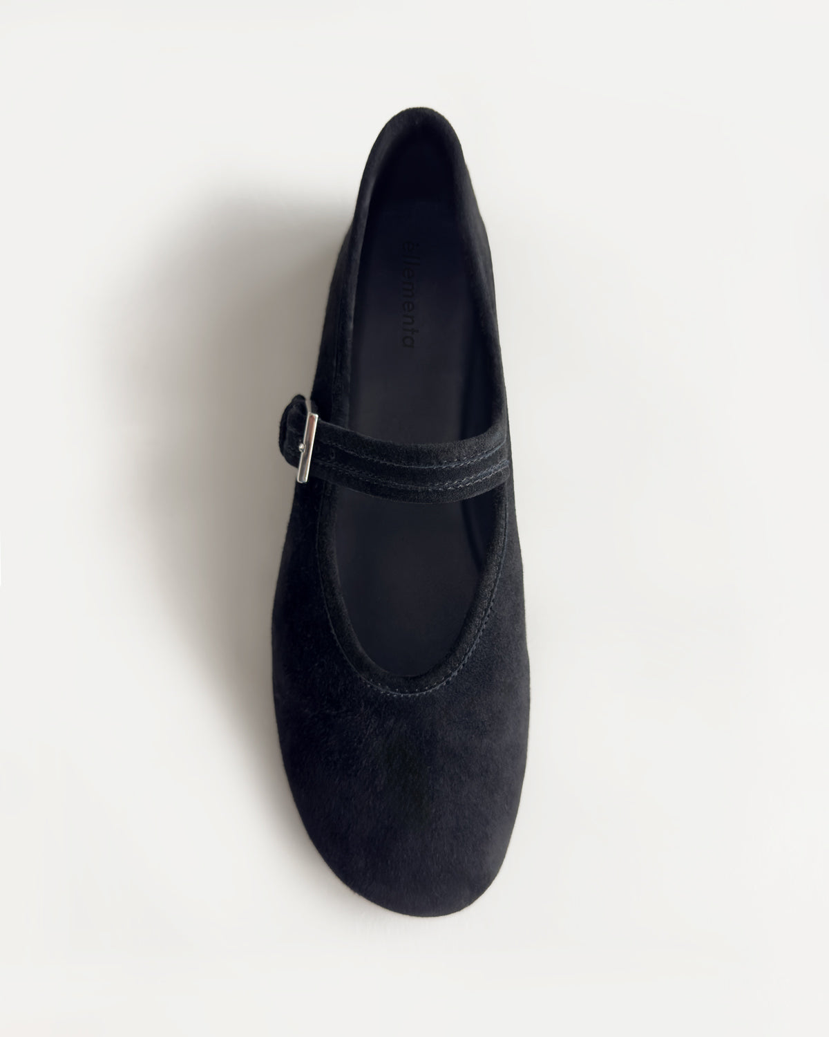 A single black suede Mary Jane shoe with a small silver buckle, photographed from a top-down angle on a clean white background.