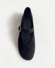 A single black suede Mary Jane shoe with a small silver buckle, photographed from a top-down angle on a clean white background.