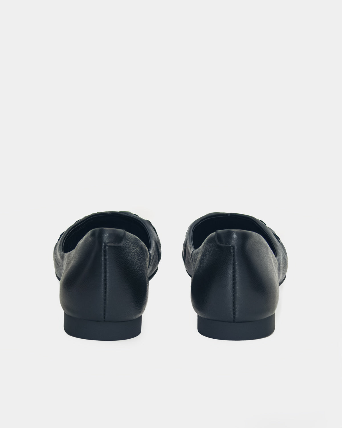 A pair of black leather flat shoes shown from the back against a light gray background.