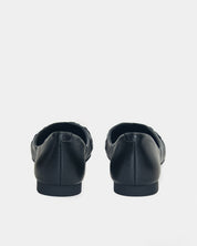 A pair of black leather flat shoes shown from the back against a light gray background.