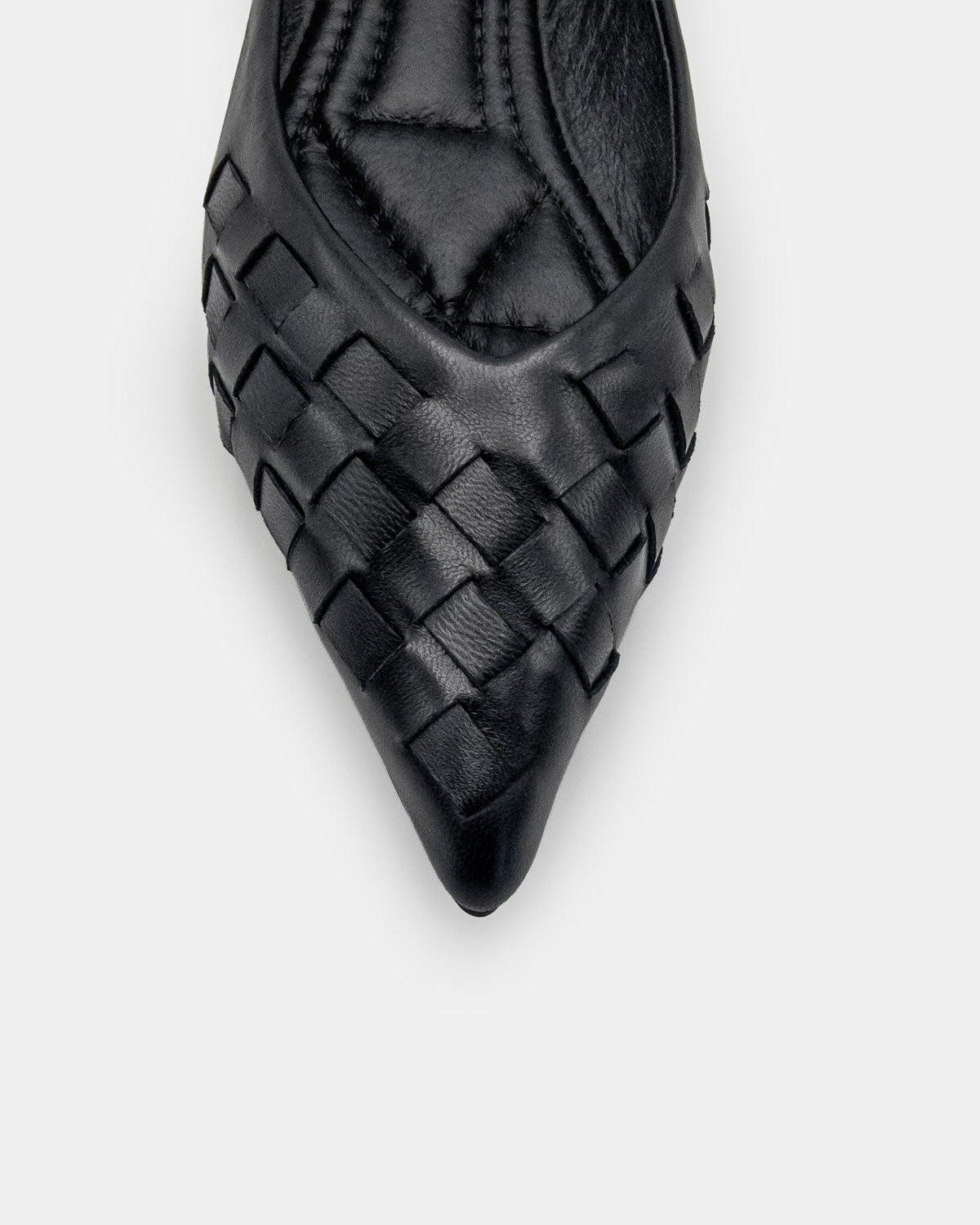 A close-up top-down view of a black leather pointed-toe flat shoe with a woven pattern on the toe box