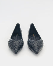 A pair of black pointed-toe flats with a woven leather upper, shown from a top-down view on a light gray background.