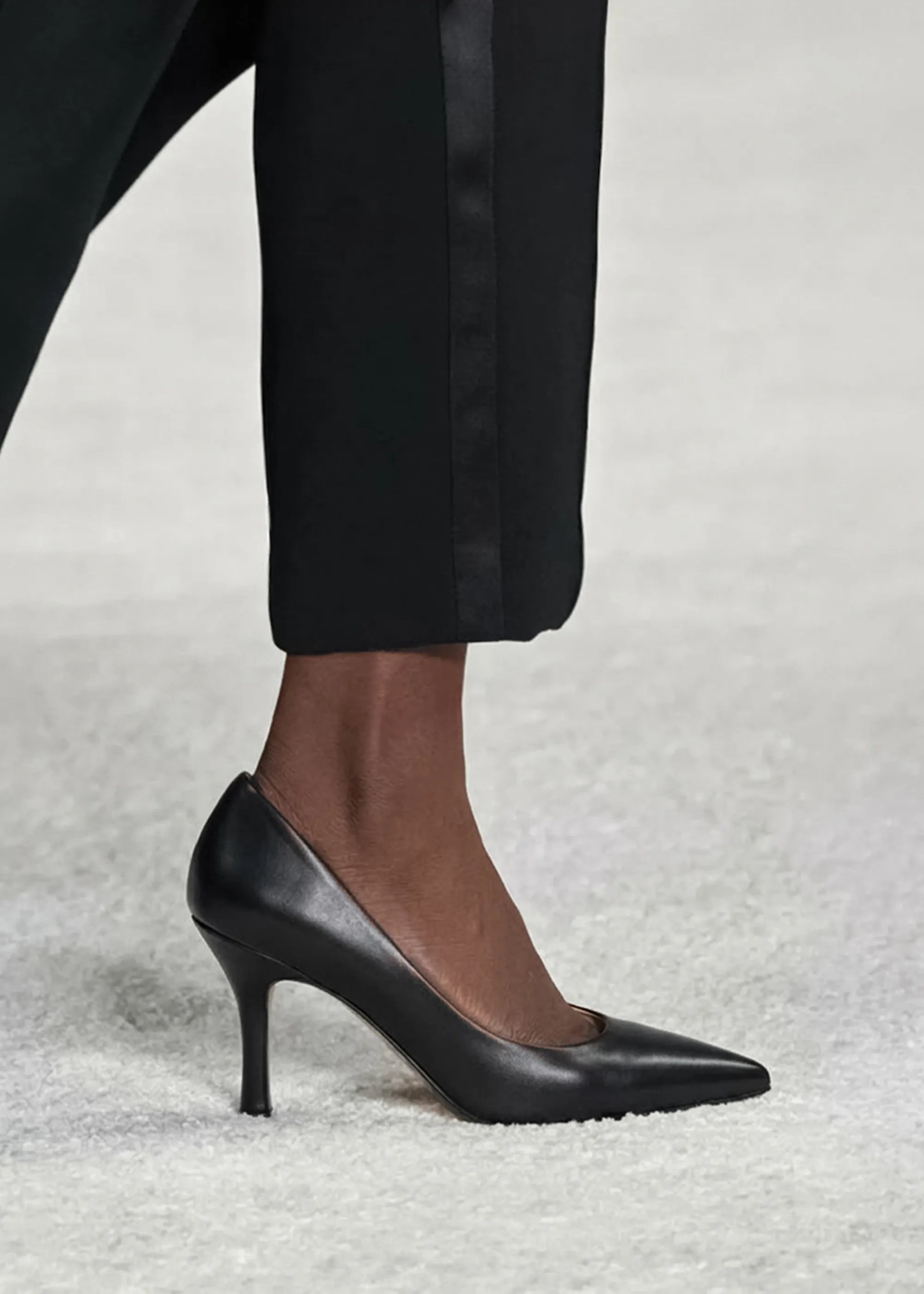 Black high-heeled shoes worn with black pants on a light gray background