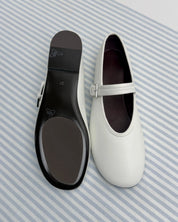 A pair of white leather Mary Jane ballet flats shown from the top and sole, displayed on a blue and white striped fabric background.
