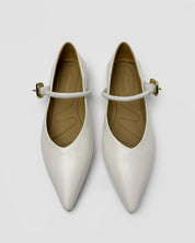A pair of pointed-toe Mary Jane flats in a glossy off-white finish, featuring a thin strap with a small gold-tone buckle, photographed from a top-down angle on a light gray background.