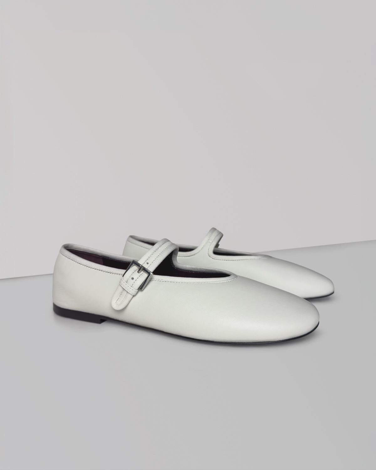 A pair of white leather Mary Jane flats with a single strap and a silver buckle, displayed on a light gray studio background.