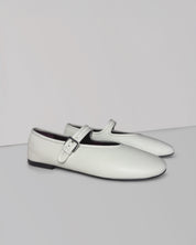 A pair of white leather Mary Jane flats with a single strap and a silver buckle, displayed on a light gray studio background.