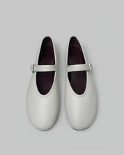 A pair of white leather Mary Jane shoes with a single strap and a small silver buckle, displayed on a neutral gray background.