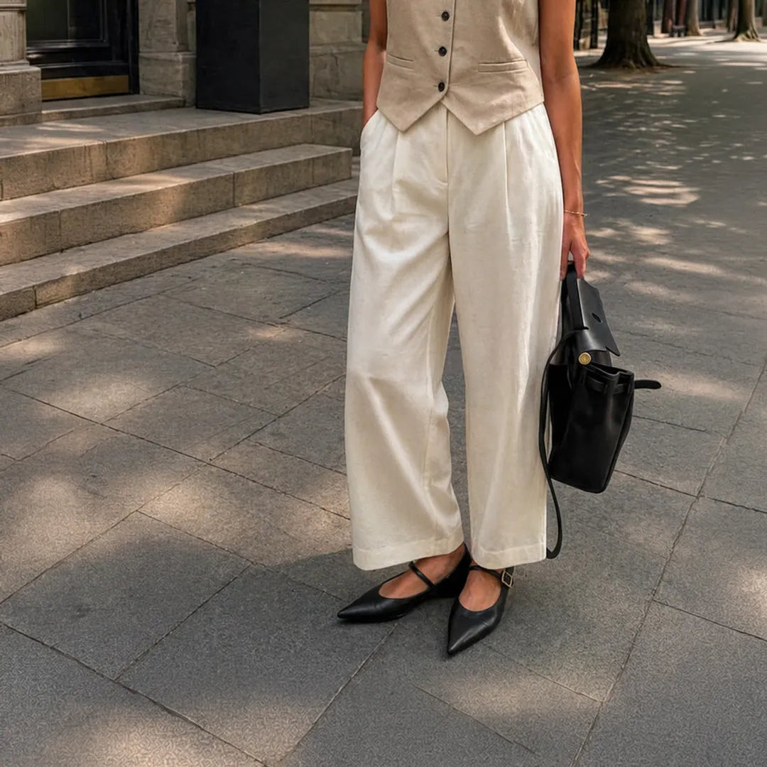 Person wearing a beige vest, white pants, and black Mary Jane flat shoes