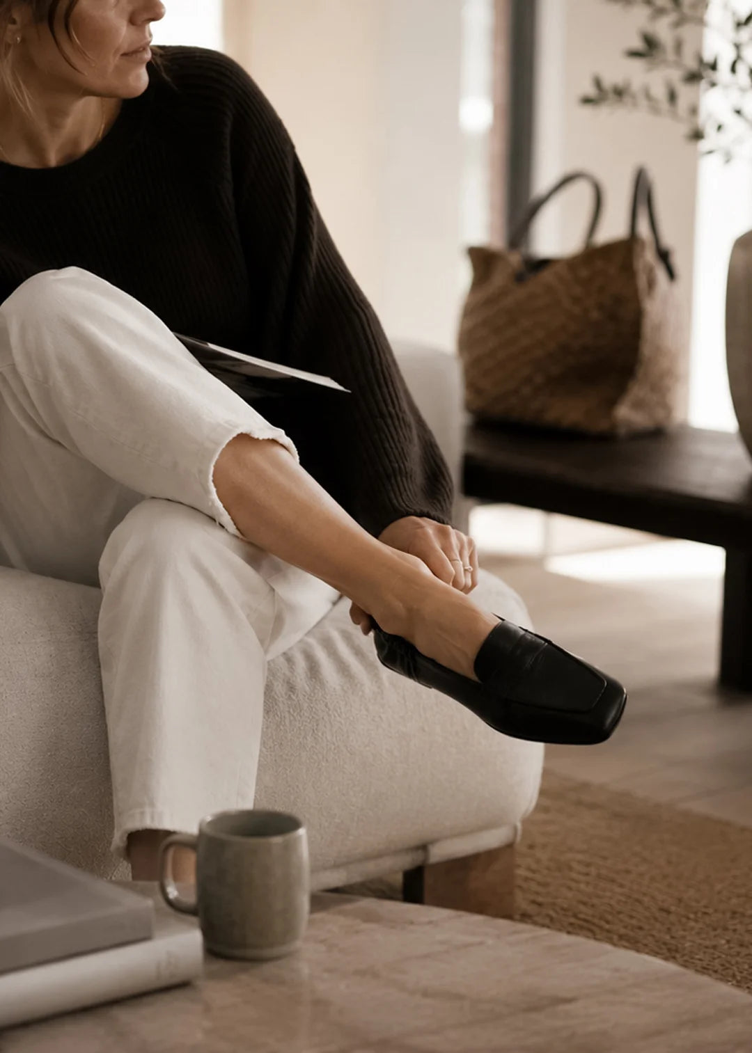 Person sitting on a couch in black loafer in a cozy living room.