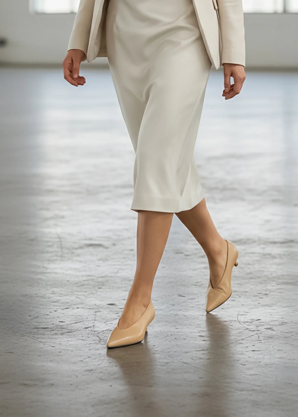 Woman wearing beige pointed toe heels and suit on a grey floor